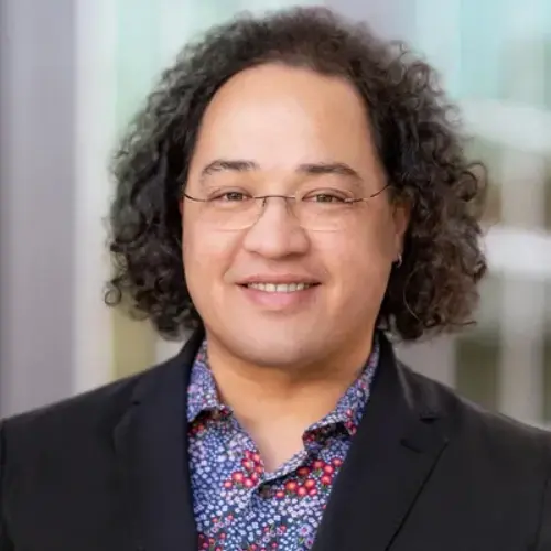 A man with curly hair and glasses is smiling.